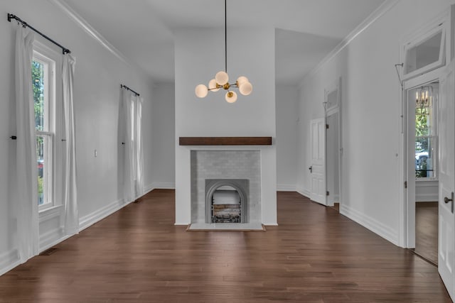 unfurnished living room featuring a fireplace, an inviting chandelier, a wealth of natural light, and dark wood-type flooring