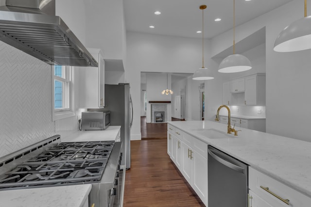 kitchen featuring wall chimney range hood, sink, light stone countertops, appliances with stainless steel finishes, and decorative light fixtures