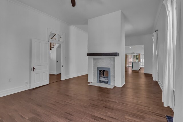 unfurnished living room featuring a fireplace, ceiling fan, crown molding, and dark wood-type flooring