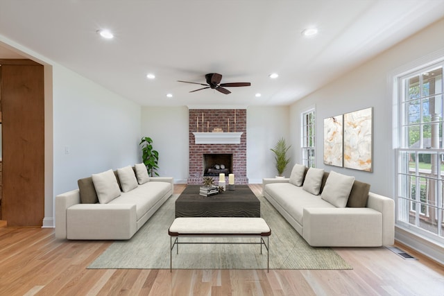 living room featuring light hardwood / wood-style floors, ceiling fan, and a brick fireplace