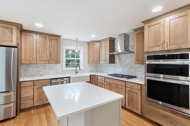 kitchen with appliances with stainless steel finishes, pendant lighting, a center island, light hardwood / wood-style flooring, and wall chimney range hood