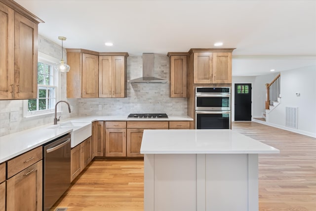 kitchen with pendant lighting, wall chimney exhaust hood, backsplash, appliances with stainless steel finishes, and light wood-type flooring