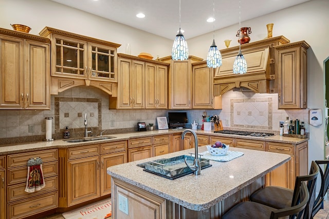 kitchen with a breakfast bar area, stainless steel gas stovetop, an island with sink, sink, and decorative light fixtures