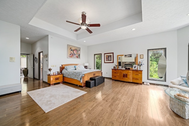 bedroom featuring wood-type flooring, a textured ceiling, a raised ceiling, and ceiling fan