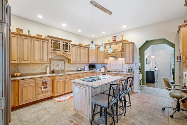 kitchen with tasteful backsplash, a kitchen island with sink, sink, and decorative light fixtures