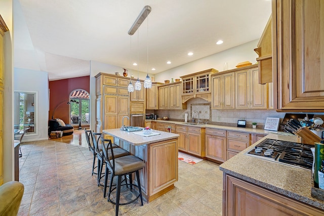 kitchen with a kitchen breakfast bar, backsplash, decorative light fixtures, a center island with sink, and sink