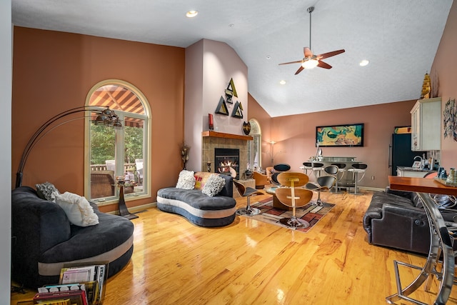 living room featuring ceiling fan, light hardwood / wood-style flooring, a tiled fireplace, and high vaulted ceiling