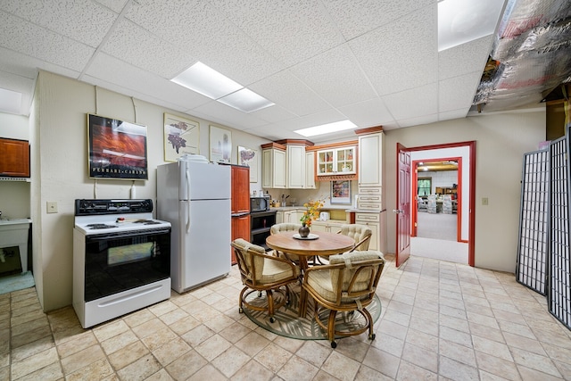 kitchen featuring white appliances, a drop ceiling, and white cabinets