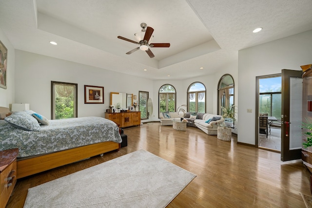 bedroom featuring a tray ceiling, ceiling fan, hardwood / wood-style flooring, and a textured ceiling