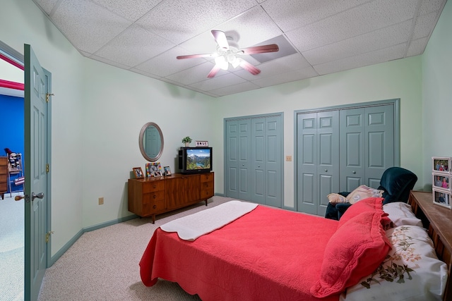 carpeted bedroom with ceiling fan, multiple closets, and a drop ceiling