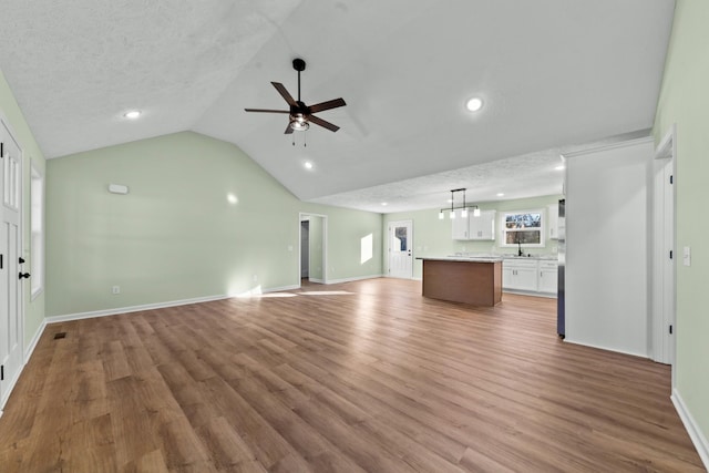 unfurnished living room with vaulted ceiling, light wood finished floors, a textured ceiling, and a ceiling fan