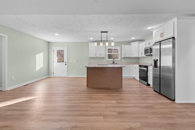 kitchen featuring a center island, light wood finished floors, appliances with stainless steel finishes, white cabinets, and a textured ceiling