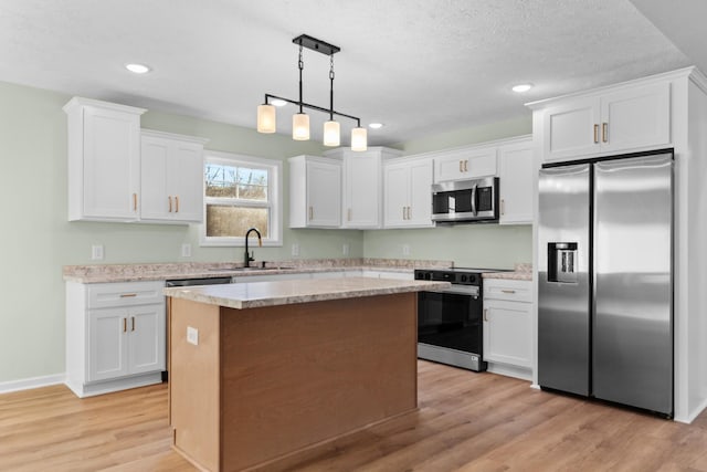 kitchen with appliances with stainless steel finishes, a center island, light wood-type flooring, white cabinetry, and a sink