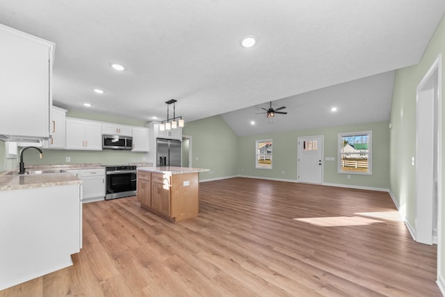 kitchen with lofted ceiling, a sink, appliances with stainless steel finishes, a center island, and light wood finished floors