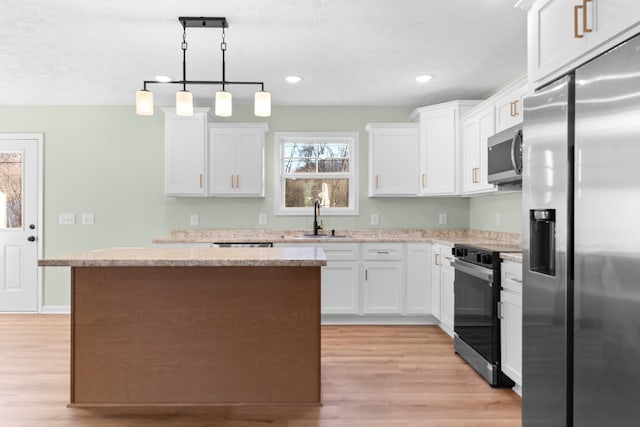 kitchen with stainless steel appliances, a kitchen island, a sink, white cabinets, and light wood finished floors