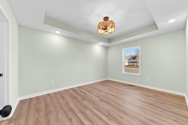 empty room with a tray ceiling, visible vents, light wood-style flooring, and baseboards