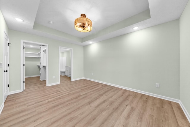 unfurnished bedroom with light wood-style flooring, a spacious closet, baseboards, and a raised ceiling