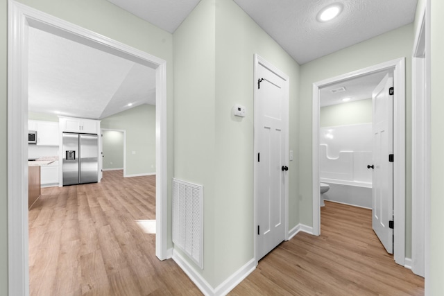 corridor featuring baseboards, vaulted ceiling, visible vents, and light wood-style floors