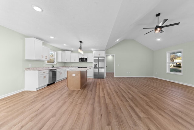 kitchen with light countertops, appliances with stainless steel finishes, open floor plan, a sink, and a kitchen island