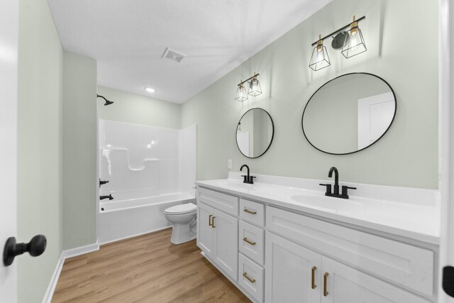 bathroom featuring double vanity, shower / bath combination, toilet, a sink, and wood finished floors