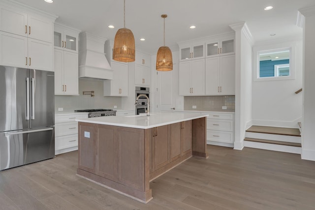 kitchen featuring custom range hood, wood finished floors, stainless steel appliances, light countertops, and white cabinetry