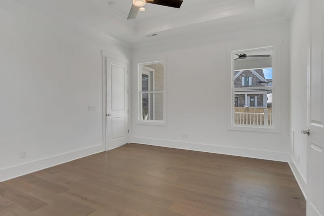 empty room featuring ceiling fan, wood finished floors, baseboards, a raised ceiling, and crown molding