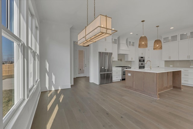 kitchen with premium appliances, premium range hood, light countertops, light wood-type flooring, and glass insert cabinets