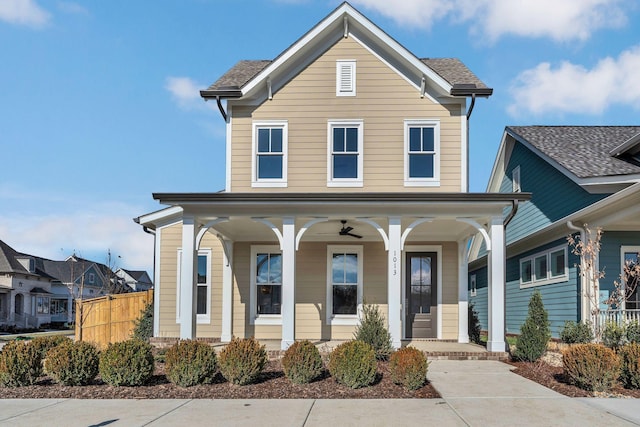 traditional home with covered porch, a shingled roof, and fence