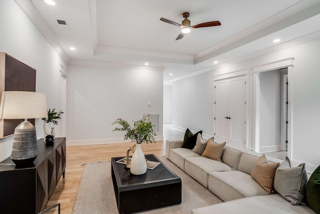 living room with light hardwood / wood-style flooring, a tray ceiling, ceiling fan, and ornamental molding