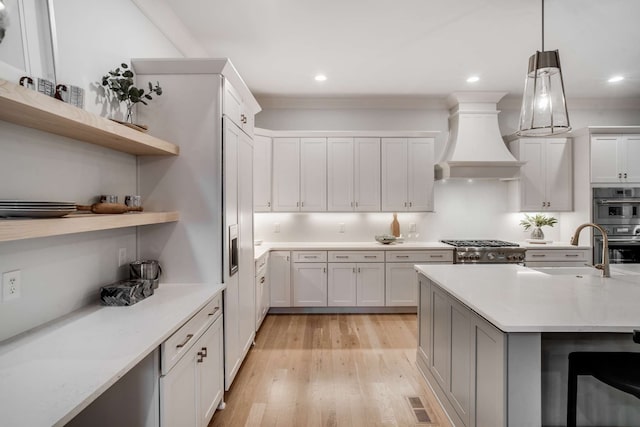 kitchen featuring pendant lighting, light wood-type flooring, white cabinets, custom exhaust hood, and appliances with stainless steel finishes