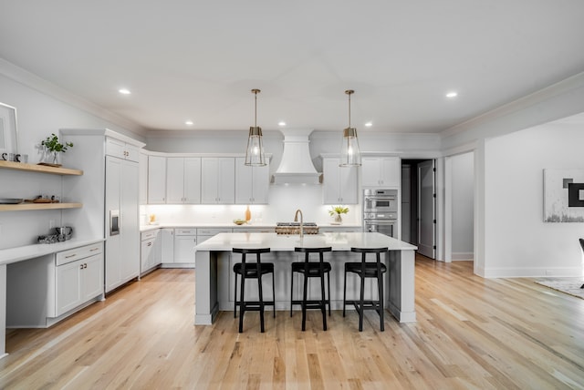 kitchen featuring premium range hood, white cabinetry, stainless steel double oven, light wood-type flooring, and a kitchen bar