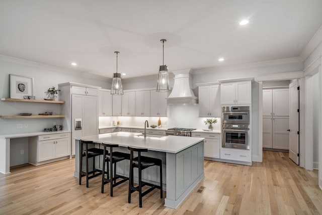 kitchen with a breakfast bar, white cabinets, stainless steel appliances, light wood-type flooring, and premium range hood