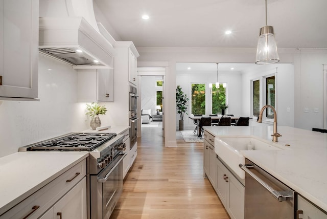 kitchen with custom range hood, hanging light fixtures, appliances with stainless steel finishes, white cabinets, and light hardwood / wood-style flooring