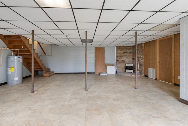 basement featuring water heater, a drop ceiling, wood walls, and heating unit