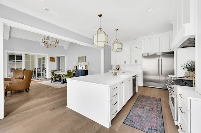 kitchen featuring light hardwood / wood-style floors, a kitchen island with sink, white cabinetry, appliances with stainless steel finishes, and decorative light fixtures