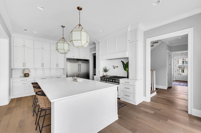 kitchen featuring wood-type flooring, a kitchen island with sink, high end appliances, and white cabinetry