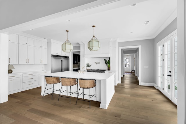 kitchen with pendant lighting, white cabinetry, high end refrigerator, a center island with sink, and dark hardwood / wood-style flooring