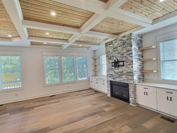 unfurnished living room featuring a healthy amount of sunlight, a large fireplace, coffered ceiling, and hardwood / wood-style floors