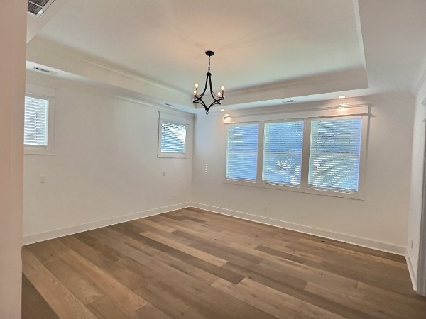 unfurnished room with a notable chandelier, a raised ceiling, and hardwood / wood-style floors