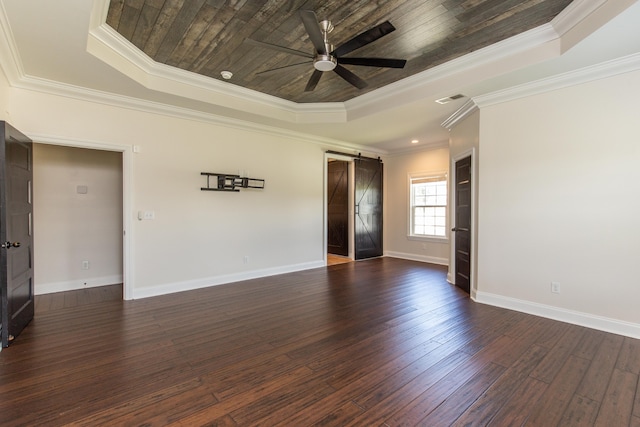 spare room featuring ornamental molding, a tray ceiling, dark wood-type flooring, and a barn door