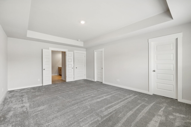 unfurnished bedroom featuring dark carpet, connected bathroom, and a tray ceiling