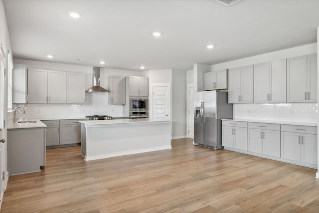 kitchen featuring appliances with stainless steel finishes, a kitchen island, wall chimney range hood, and light hardwood / wood-style flooring