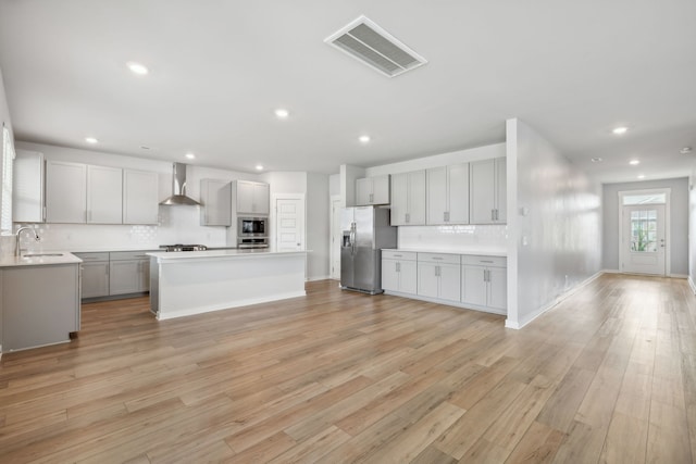 kitchen featuring gray cabinets, light wood-type flooring, a center island, wall chimney range hood, and stainless steel appliances