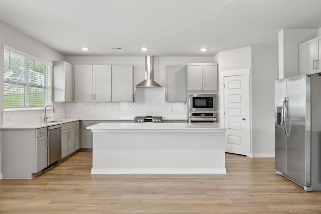 kitchen featuring a kitchen island, stainless steel appliances, light hardwood / wood-style flooring, sink, and wall chimney range hood