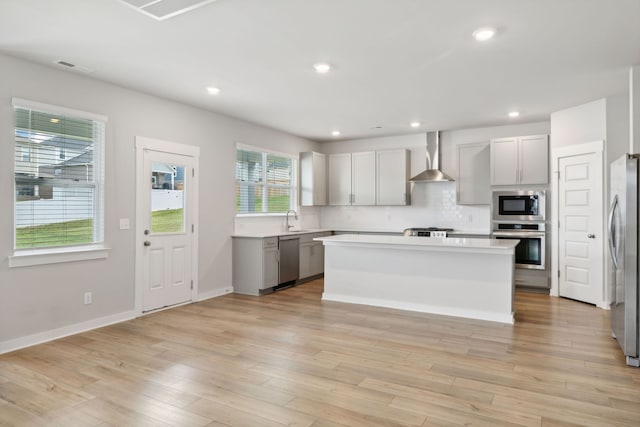 kitchen featuring gray cabinetry, wall chimney exhaust hood, stainless steel appliances, light wood-type flooring, and a center island