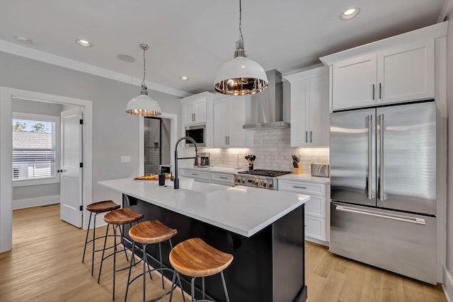 kitchen with light countertops, light wood-type flooring, wall chimney exhaust hood, decorative backsplash, and appliances with stainless steel finishes