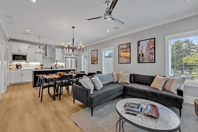 living room featuring light hardwood / wood-style flooring, ceiling fan with notable chandelier, and crown molding