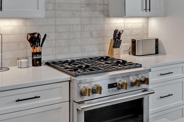 kitchen featuring light countertops, high end range, backsplash, and white cabinetry