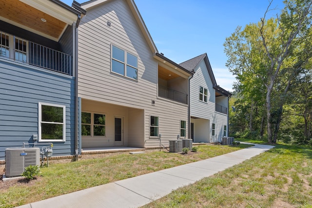 rear view of property with a lawn, a balcony, and central air condition unit