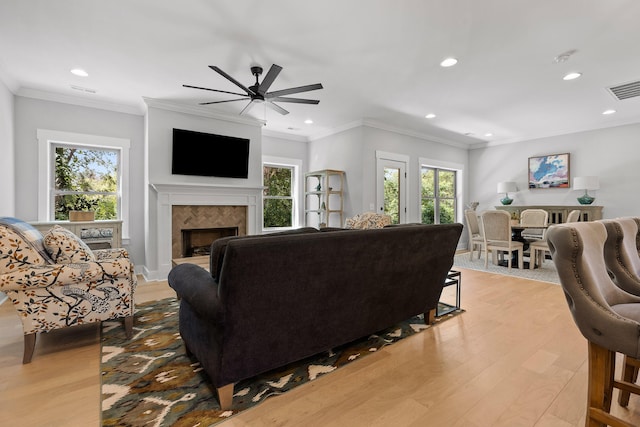 living room with light hardwood / wood-style flooring, a tiled fireplace, plenty of natural light, and ornamental molding